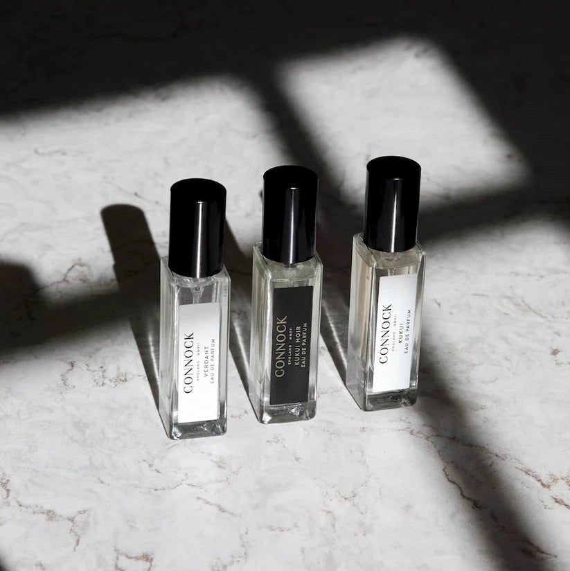 Three glass bottles with black lids standing on a marble surface with the shadow of a window over them