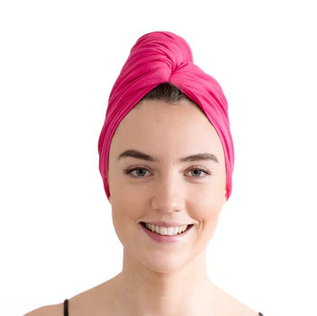 Woman wearing a bright pink hair towel wrapped around her head to resemble a turban on a white background