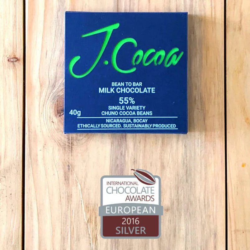 J.Cocoa milk chocolate bar packaging on a wooden surface with a silver award badge.