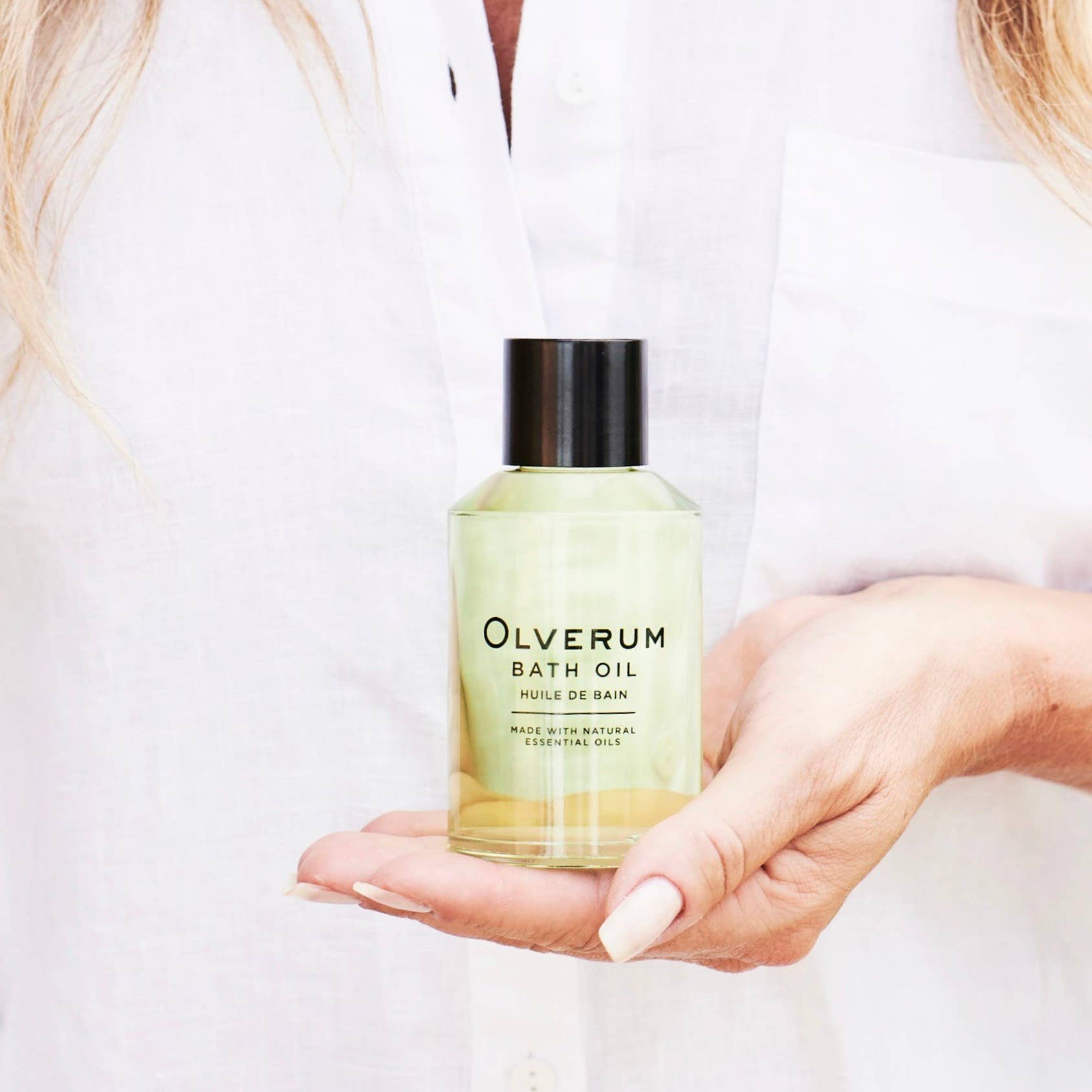 Person holding a bottle of Olverum bath oil against a white background