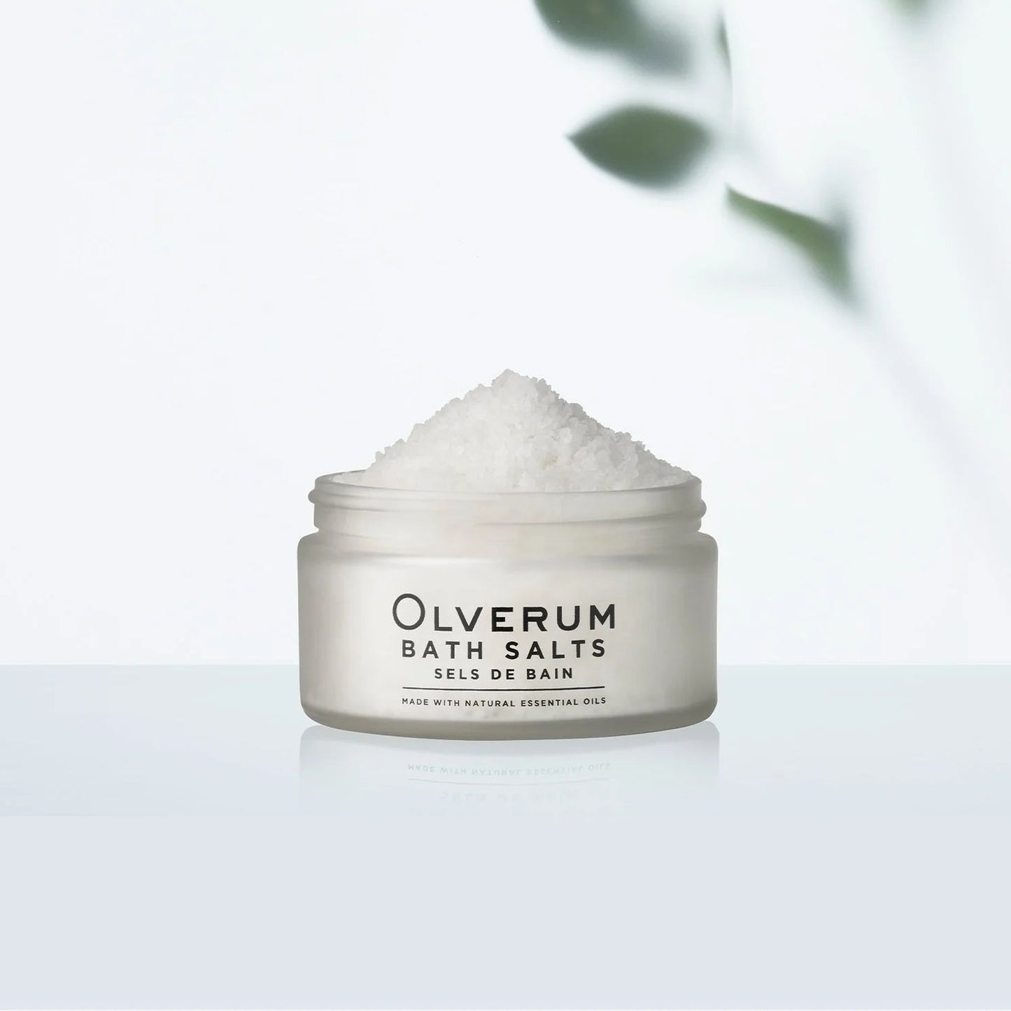 Jar of Olverum bath salts with a blurred green leafy background