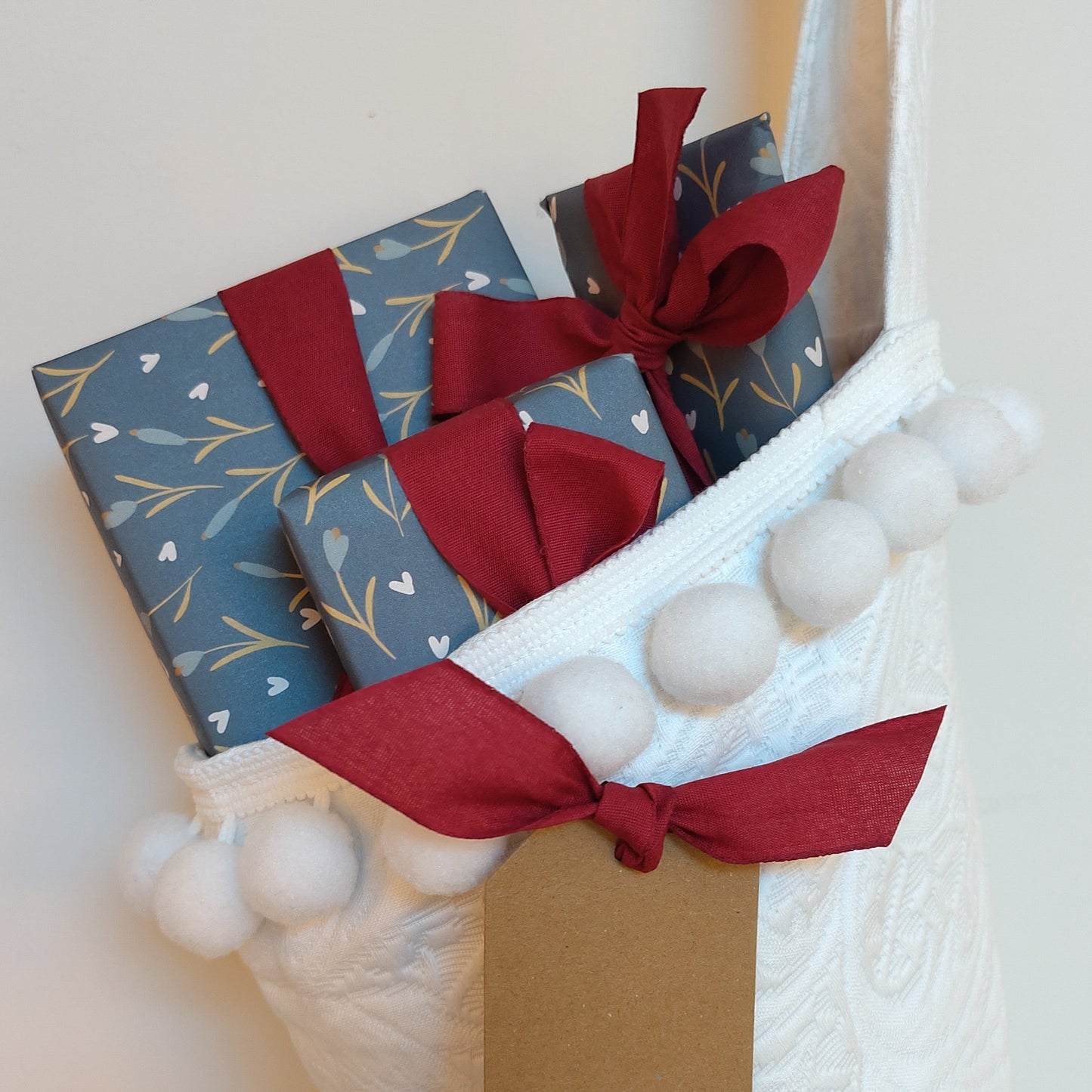 Three wrapped gifts poking out of the top of a white Christmas stocking