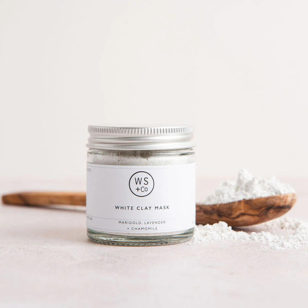 Jar of white clay mask with a wooden spoon and white clay powder on a light background