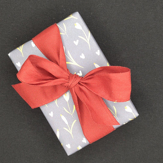 Box gift wrapped in blue paper with floral patterns and a red ribbon on a black background