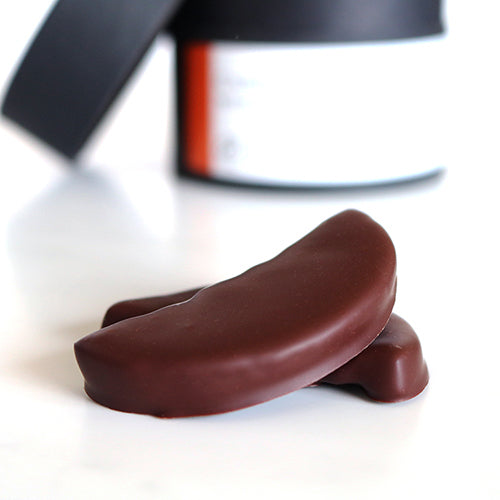 Close up of a chocolate-covered orange segment on a white surface with a blurred background