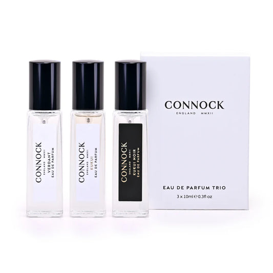 A row of 3 10ml glass bottles with black plastic lids and CONNOCK branding, standing beside a white box with black writing on it saying CONNOCK England Eau de Parfum Trio