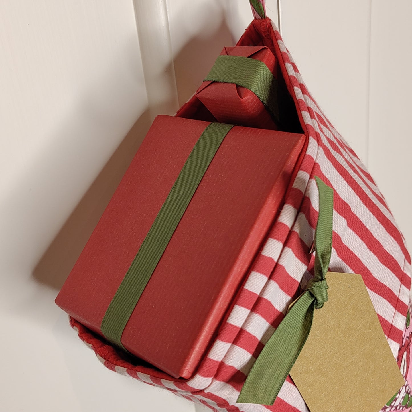 A close up shot of the top of a filled Christmas stocking with presents wrapped in red paper with green ribbon.