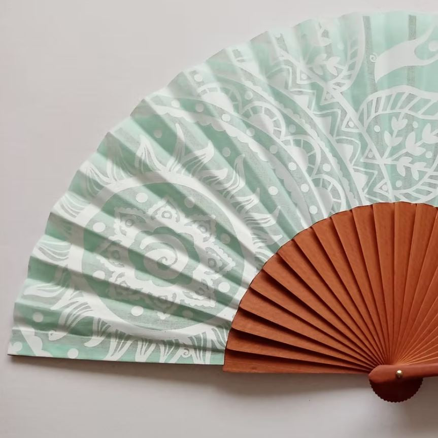 Handheld fan with green patterned cover and brown wooden handle on a light grey background
