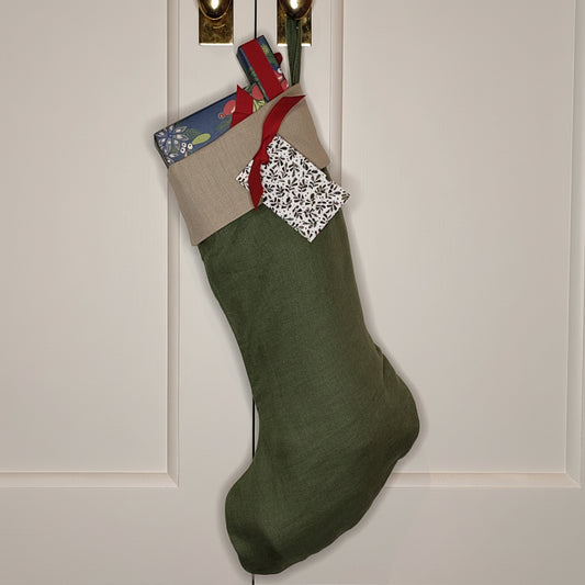 A green linen stocking with a beige cuff hanging on a cupboard door filled with presents wrapped in blue and red.