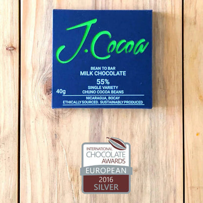 J.Cocoa milk chocolate bar packaging on a wooden surface with a silver award badge.