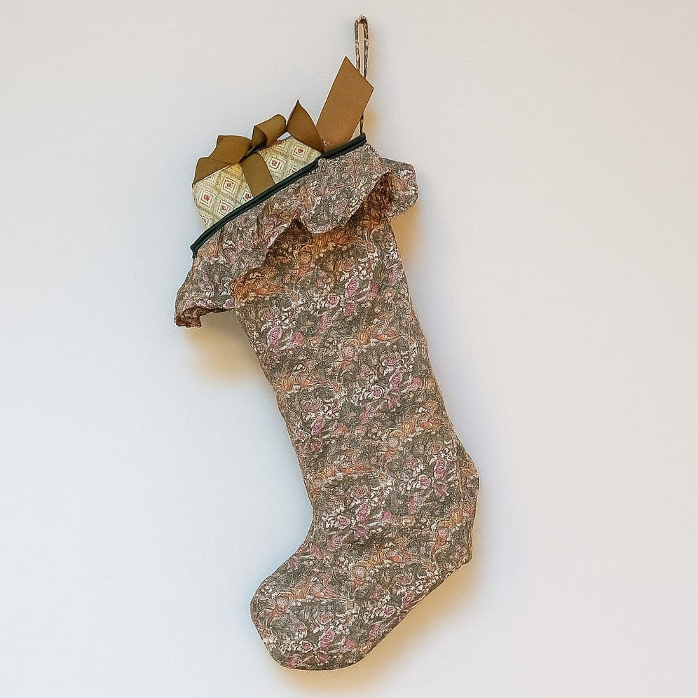 Floral-patterned Christmas stocking with a frill and full of wrapped presents on a white background