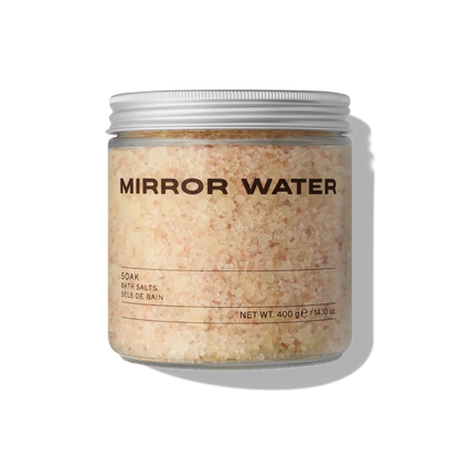 Jar of 'Mirror Water' bath salts that are slightly pink on a white background