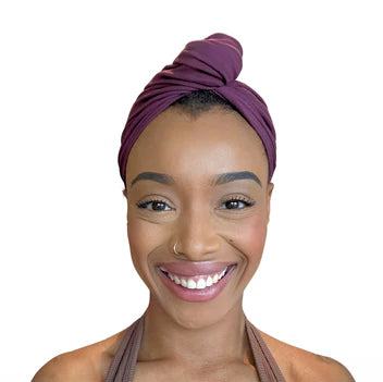 Woman wearing a purple cotton hair towel wrapped as a turban on a white background