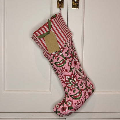 An Indian block print stocking in a red, pink and green design, hanging on a cupboard hook and filled with wrapped presents.