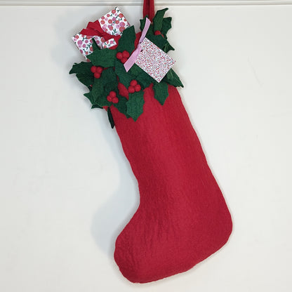 A red stocking made of felt with green felt holly leaf fringe around the the top filled with wrapped presents with red ribbon.