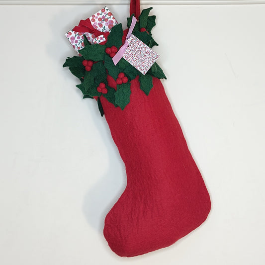 A red stocking made of felt with green felt holly leaf fringe around the the top filled with wrapped presents with red ribbon.