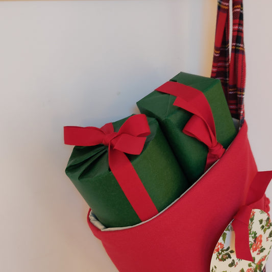 Presents wrapped in green paper and  red ribbon poking out of a Christmas stocking on a white surface