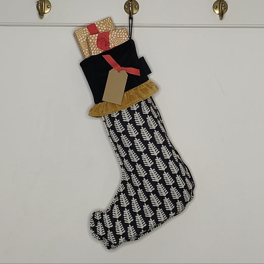 Black and white patterned Christmas stocking filled with wrapped presents hanging on a white wall.