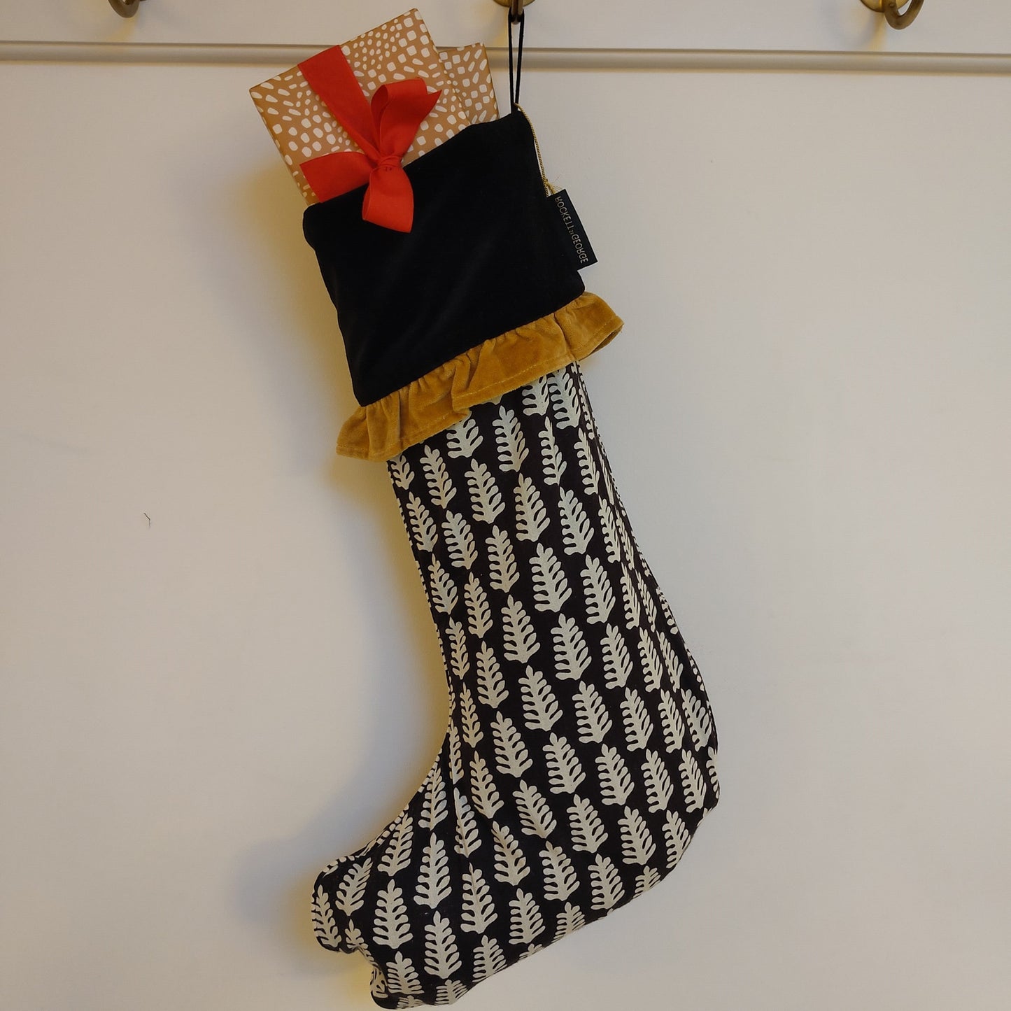 Black and white patterned Christmas stocking with a gold frill hanging on a hook with wrapped presents poking out of the top
