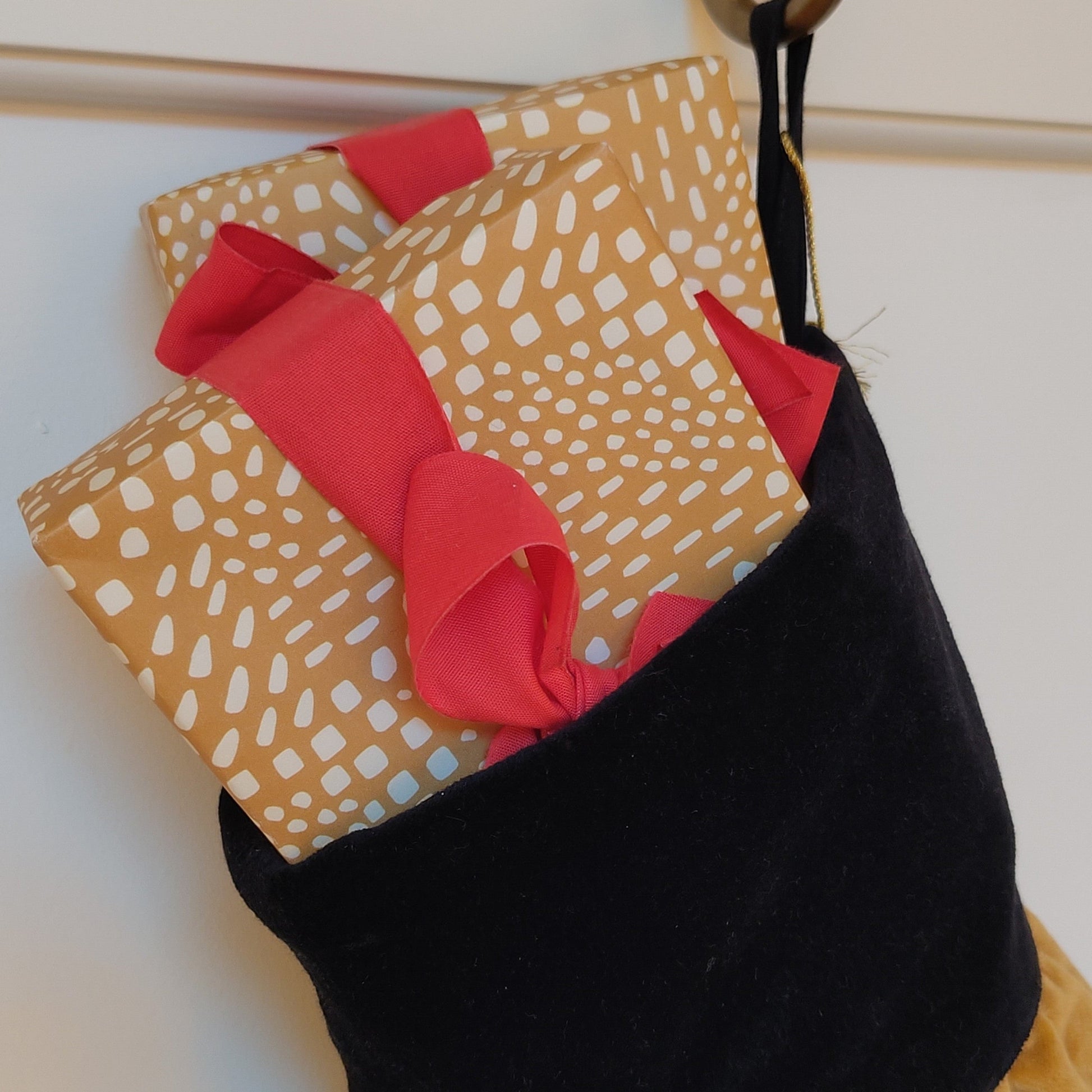 Black Christmas stocking filled with a gold patterned wrapped presents red ribbon