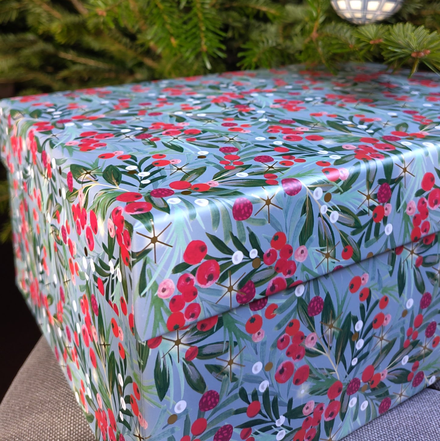 A gift box with a blue background and patterned with red berries and green leaves.