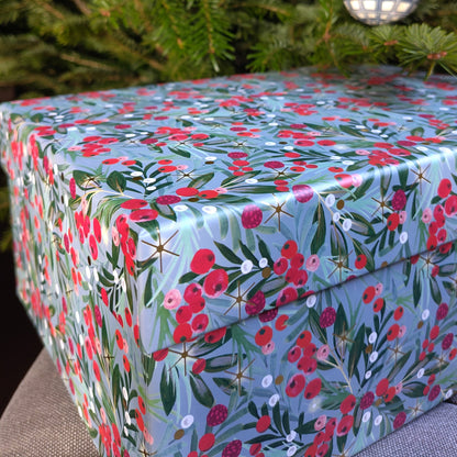 A gift box with a blue background and patterned with red berries and green leaves.