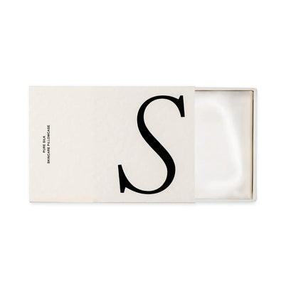 Rectangular white box with letter 'S' on a white background that is open to show a white folded silk pillowcase inside