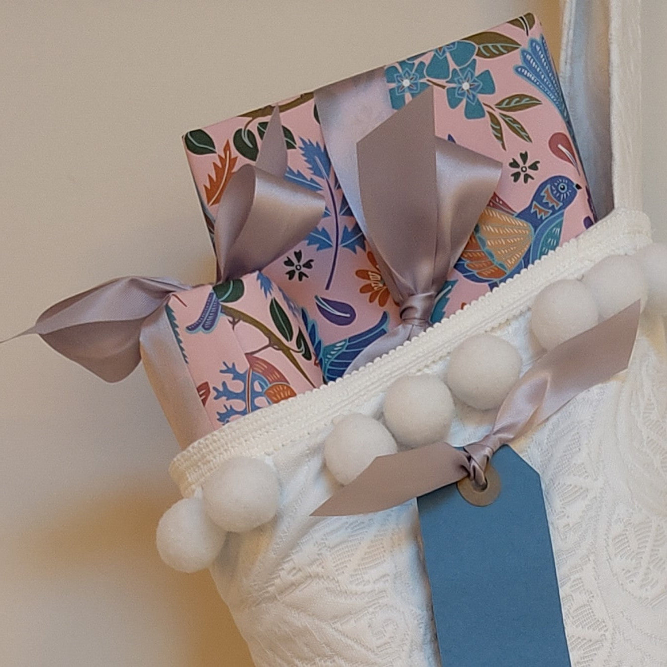 Close up of wrapped presents wrapped in paper with a floral design, ribbons, and poking out of a white Christmas stocking