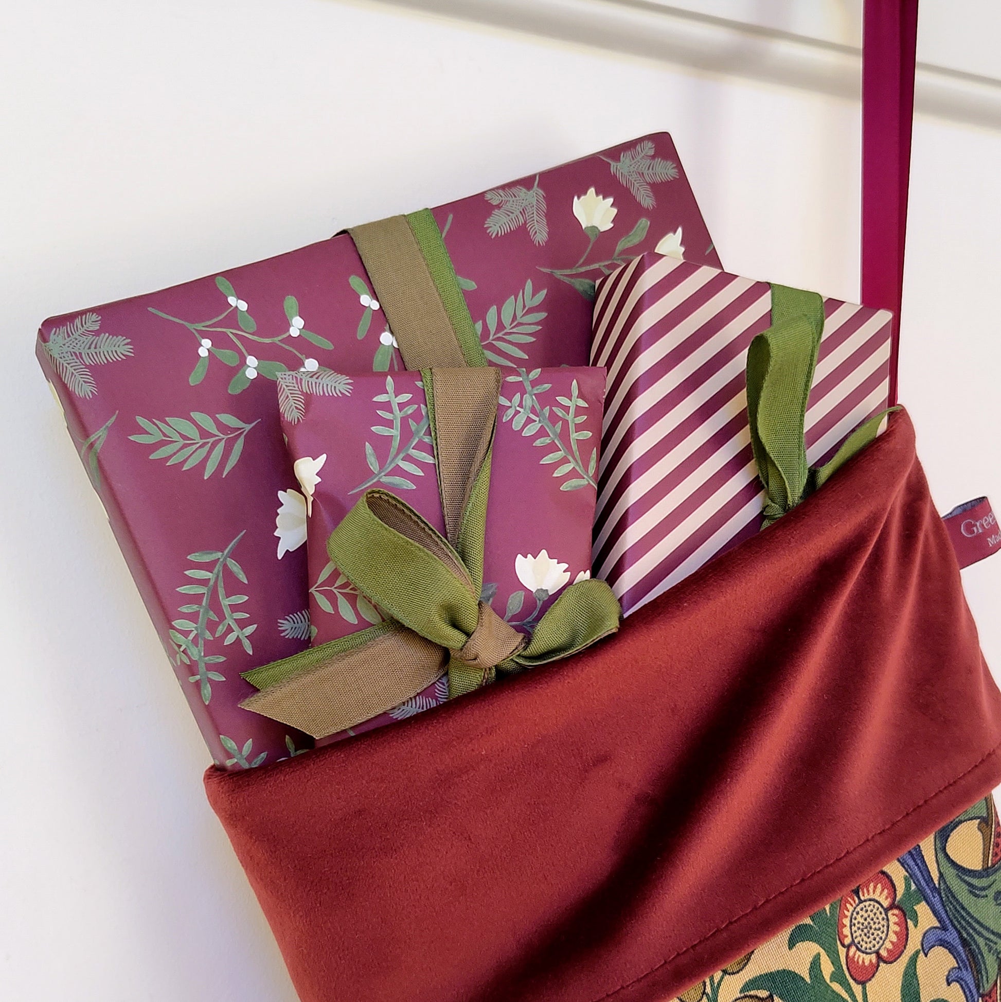Gifts wrapped in pink and green paper with ribbons poking out of the top of a Christmas stocking.